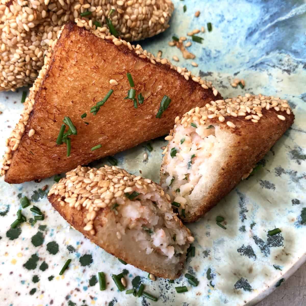 Plate of crispy golden shrimp toast triangles with one cut open revealing abundant shrimp filling inside, authentic Chinese shrimp toast appetizer.