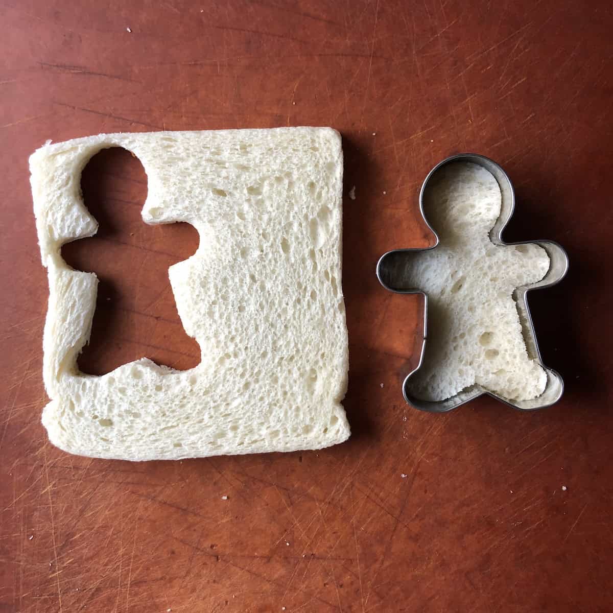 Gingerbread man cookie cutter with white bread inside and cutout bread shape beside it showing how to make Christmas-shaped shrimp on toast appetizer.
