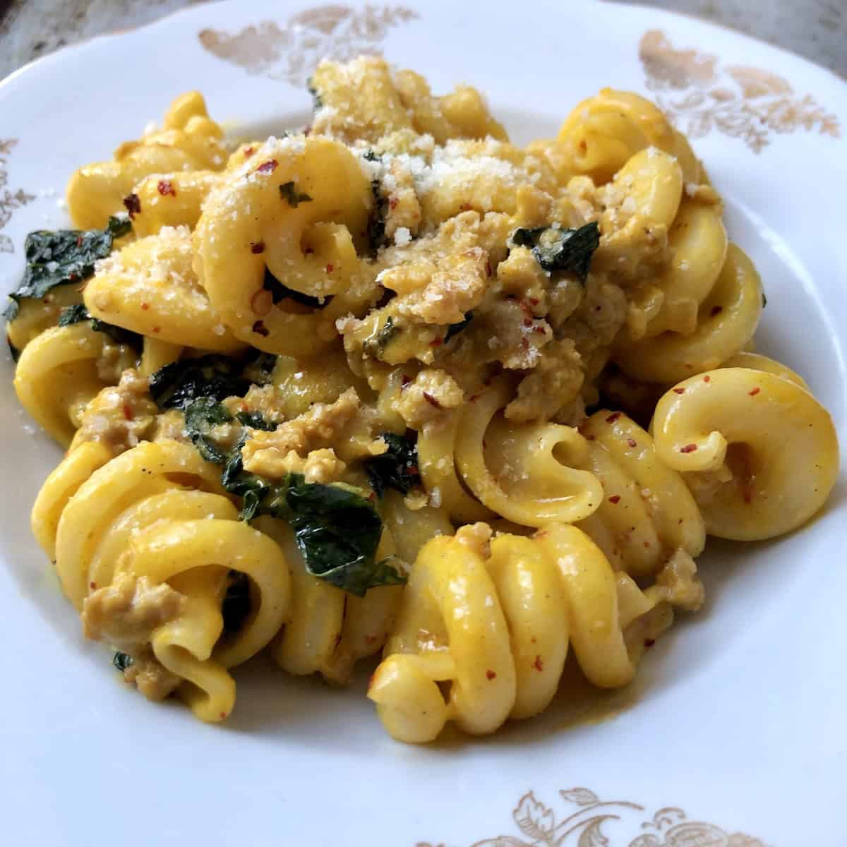 Creamy pumpkin pasta recipe served in a pasta plate topped with grated grana padano cheese, featuring sausage kale pasta in pumpkin pasta sauce.