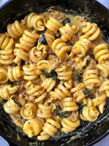Creamy pumpkin pasta with sausage and kale in a cast iron skillet featuring trottole pasta coated in pumpkin cream sauce, an easy pumpkin pasta sauce recipe.