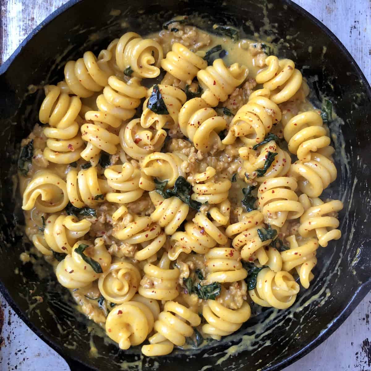Creamy pumpkin pasta with sausage and kale in a cast iron skillet featuring trottole pasta coated in pumpkin cream sauce, an easy pumpkin pasta sauce recipe.