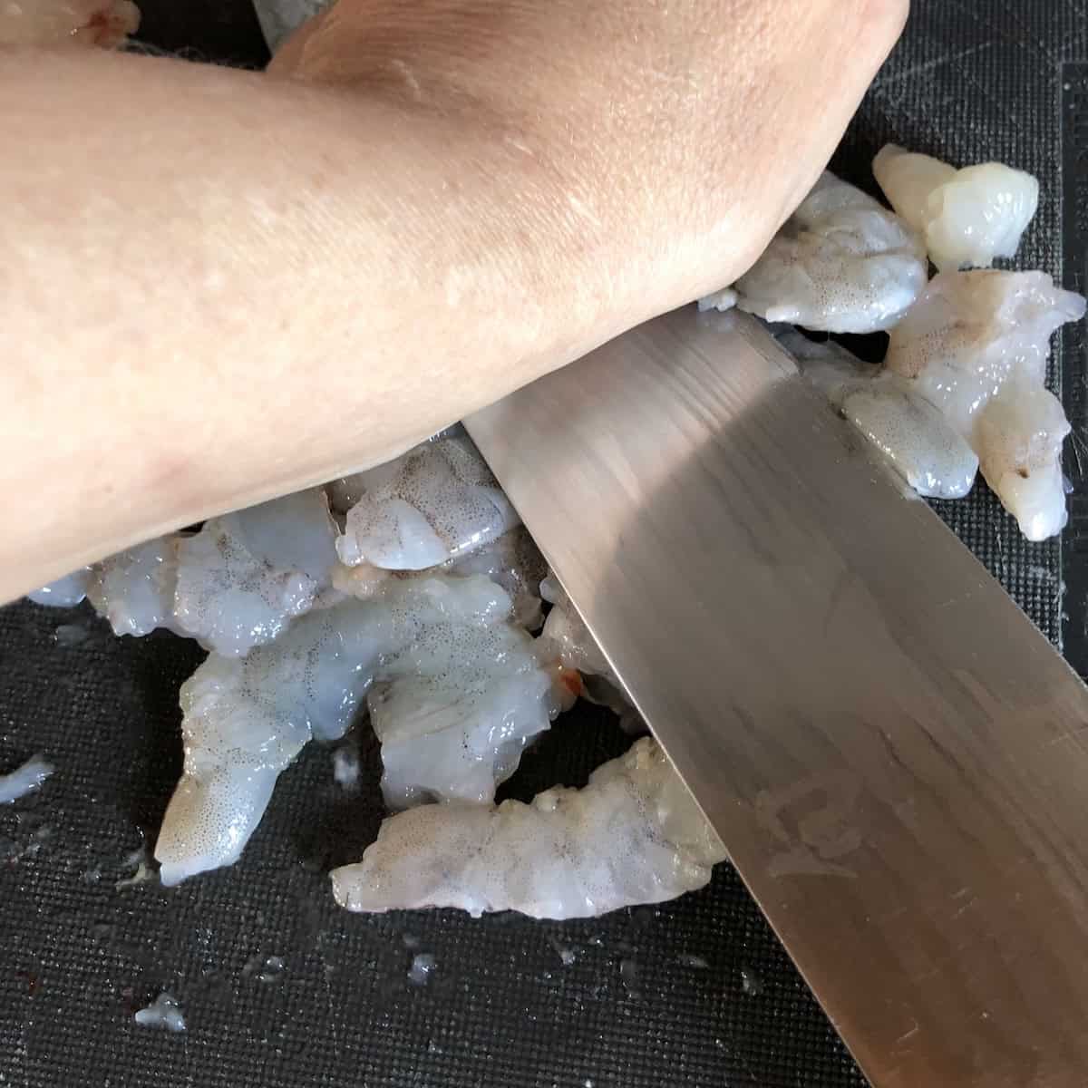 Smashing shrimp with chef knife on cutting board for traditional hand-chopped shrimp toast recipe, authentic Chinese method.