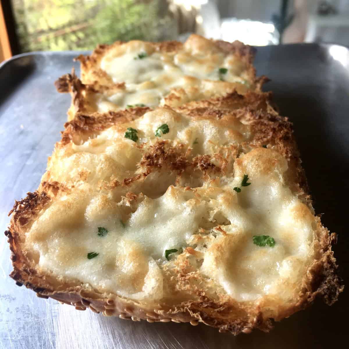 A piece of Italian bread covered with homemade mozzarella parmesan butter spread and toasted to golden brown cheesy deliciousness and sprinkled with parsley.