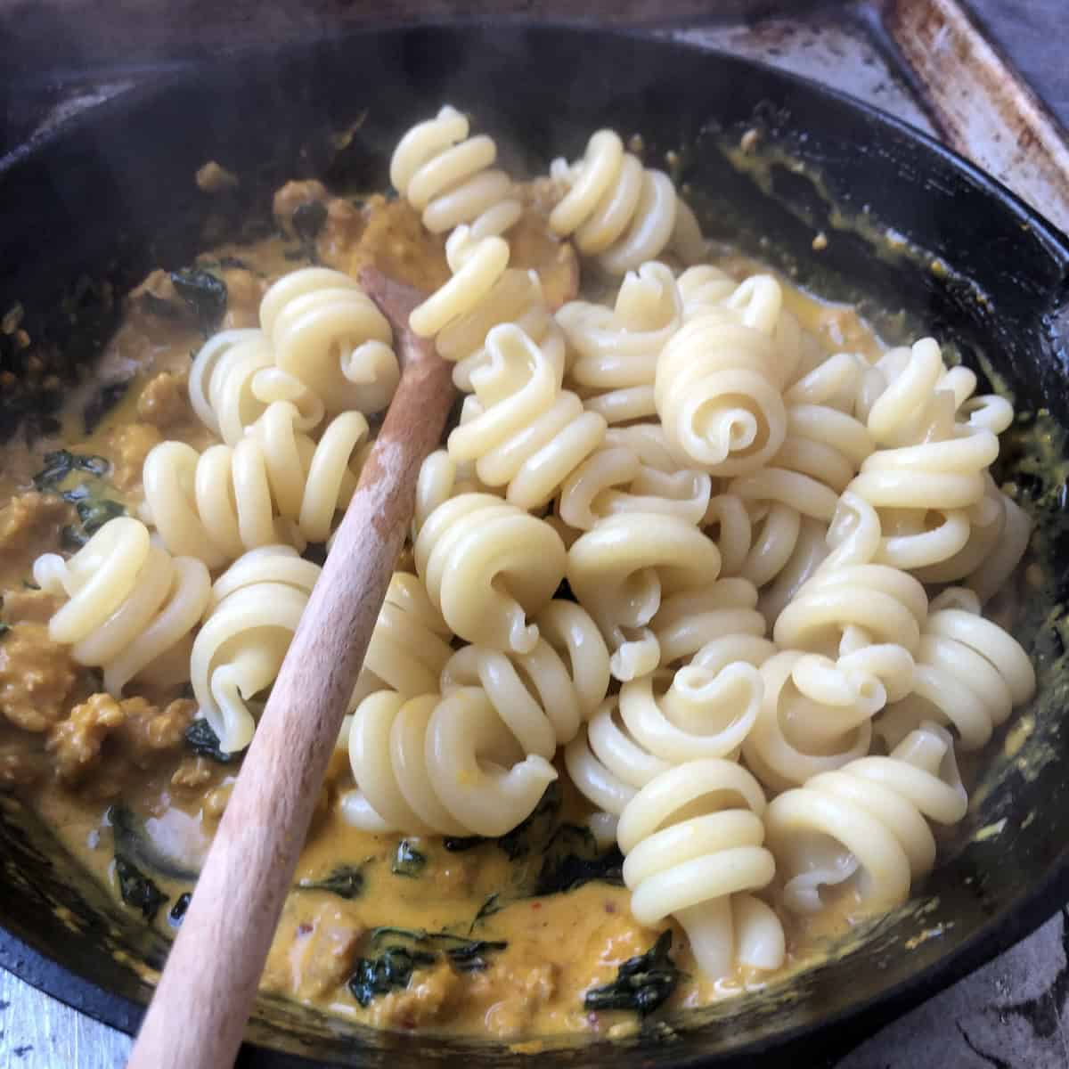 Adding trottole pasta to pumpkin pasta sauce recipe, tossing to coat in creamy pumpkin sauce for pasta.
