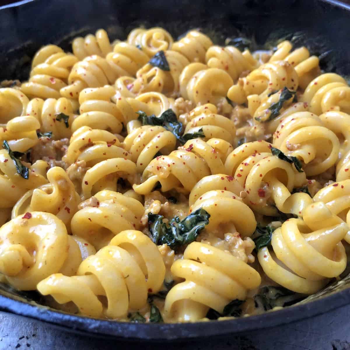 Closeup of pumpkin sauce for pasta with sausage and kale showing trottole pasta twists in creamy pumpkin cream sauce in a cast iron skillet.

