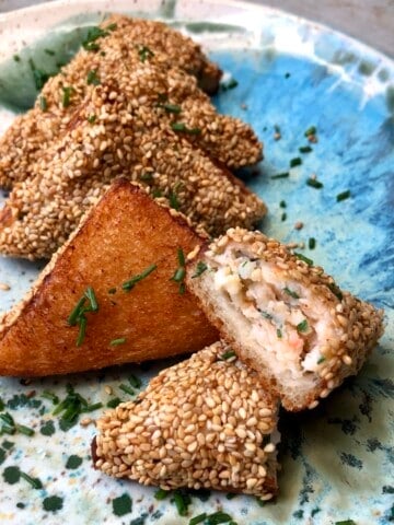 Homemade shrimp toast cut in half showing abundant shrimp filling inside, with crispy golden sesame-topped toasts on plate, authentic Chinese shrimp toast recipe appetizer.