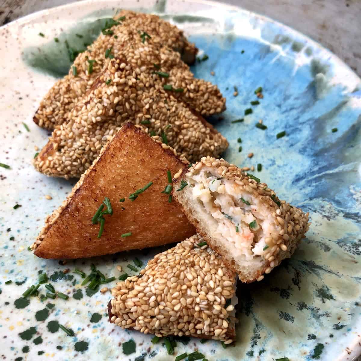 Homemade shrimp toast cut in half showing abundant shrimp filling inside, with crispy golden sesame-topped toasts on plate, authentic Chinese shrimp toast recipe appetizer.