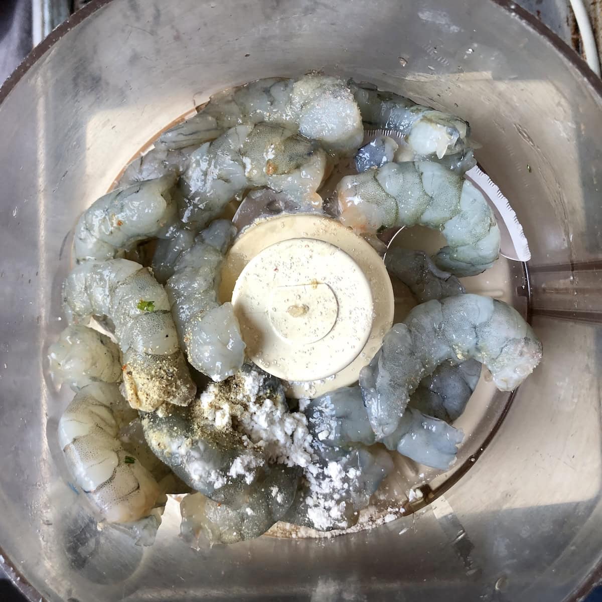 Raw shrimp with sesame oil, Shaoxing wine, salt, sugar, white pepper, and potato starch in food processor bowl for homemade shrimp toast recipe.
