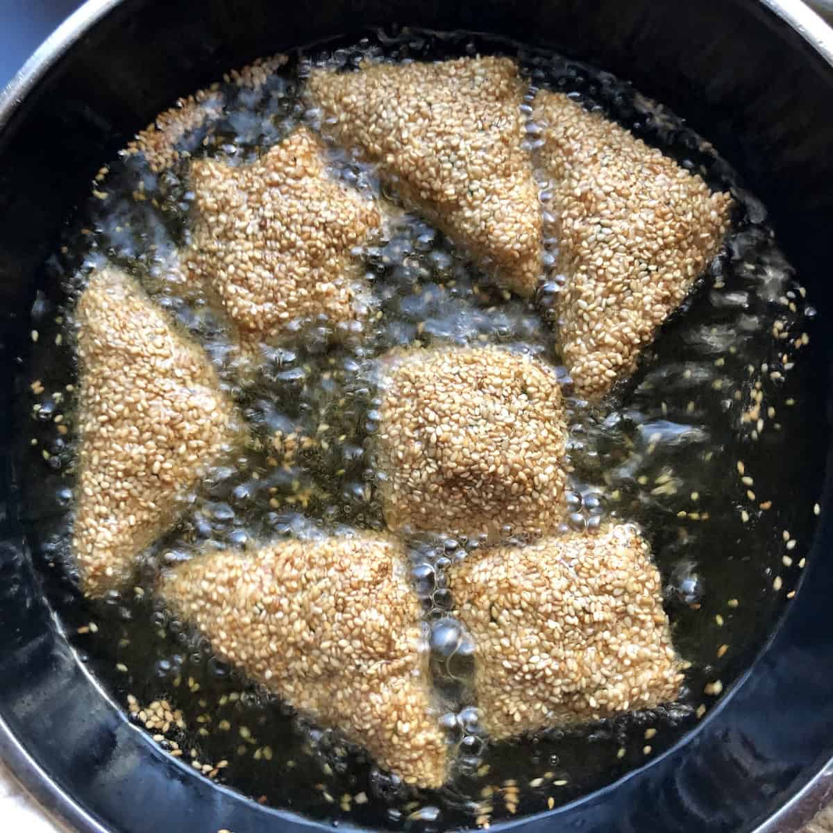 Shallow frying shrimp toasts in oil showing how to make shrimp toast crispy and golden brown in skillet.
