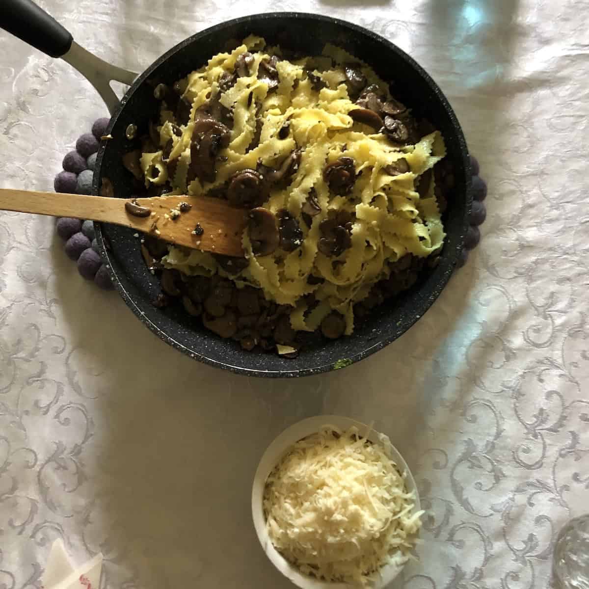 Anna's pasta ai funghi in a serving dish next to a bowl of freshly grated 30-month aged Grana Padano, an authentic Italian mushroom pasta recipe.
