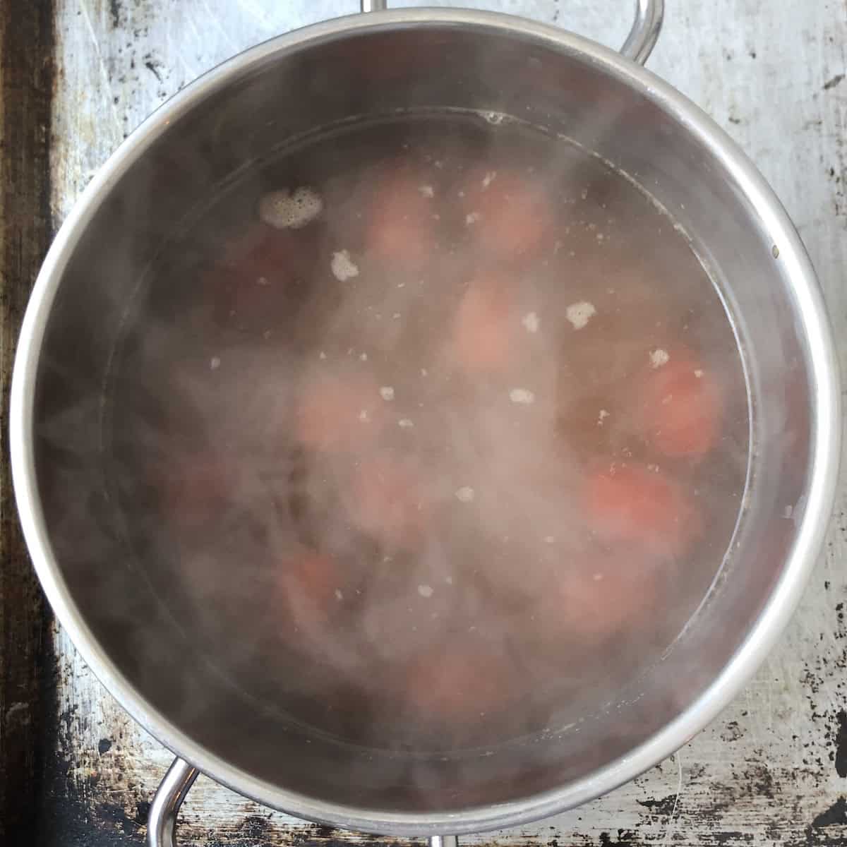 Blanching scored grape tomatoes in homemade seafood stock to remove peels for lobster tomato cream sauce recipe.
