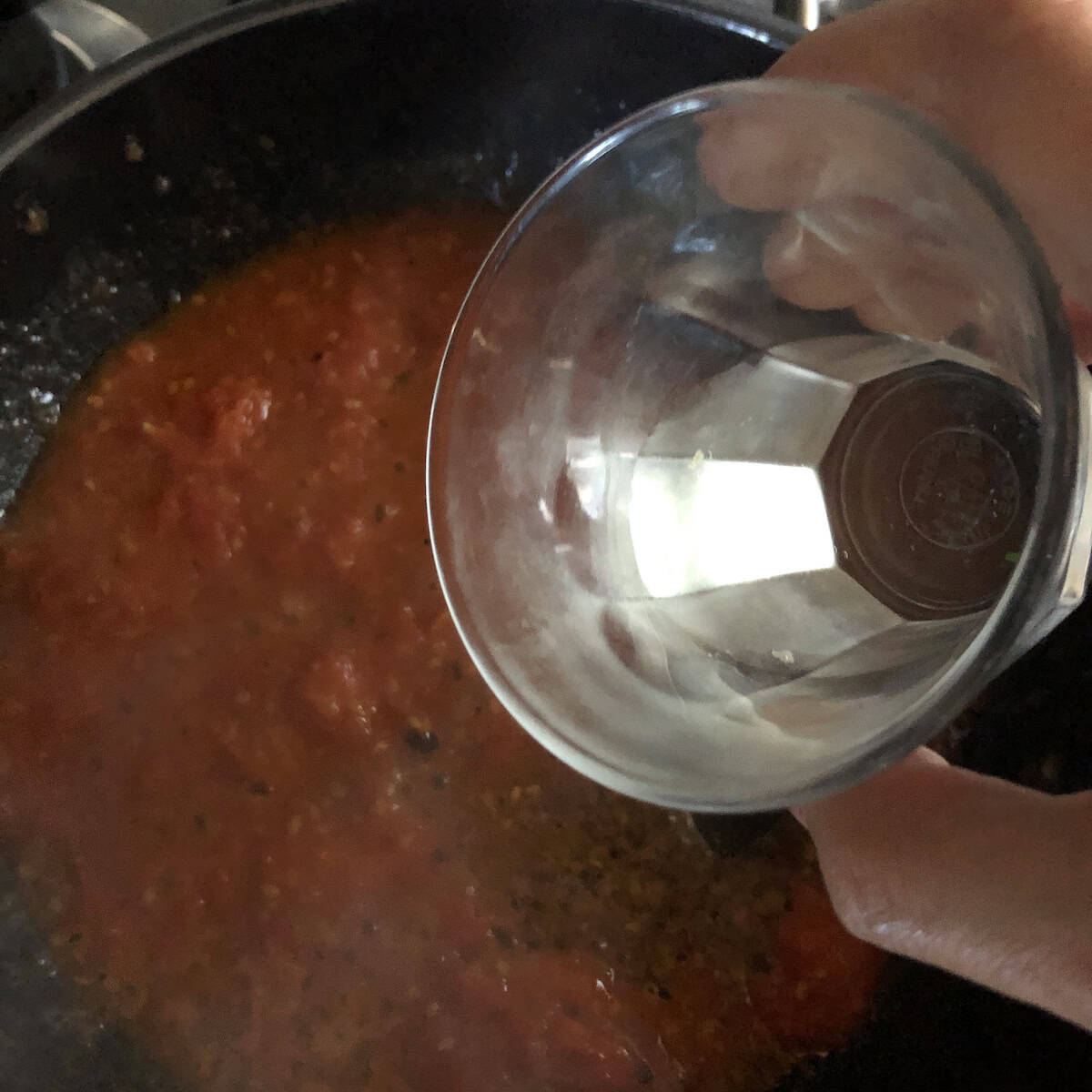 Deglazing smashed tomatoes with white wine for lobster ravioli tomato cream sauce recipe.

