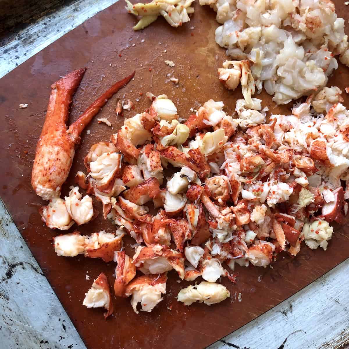 Diced cooked lobster meat on a cutting board with whole claw reserved for garnish for lobster ravioli filling recipe.
