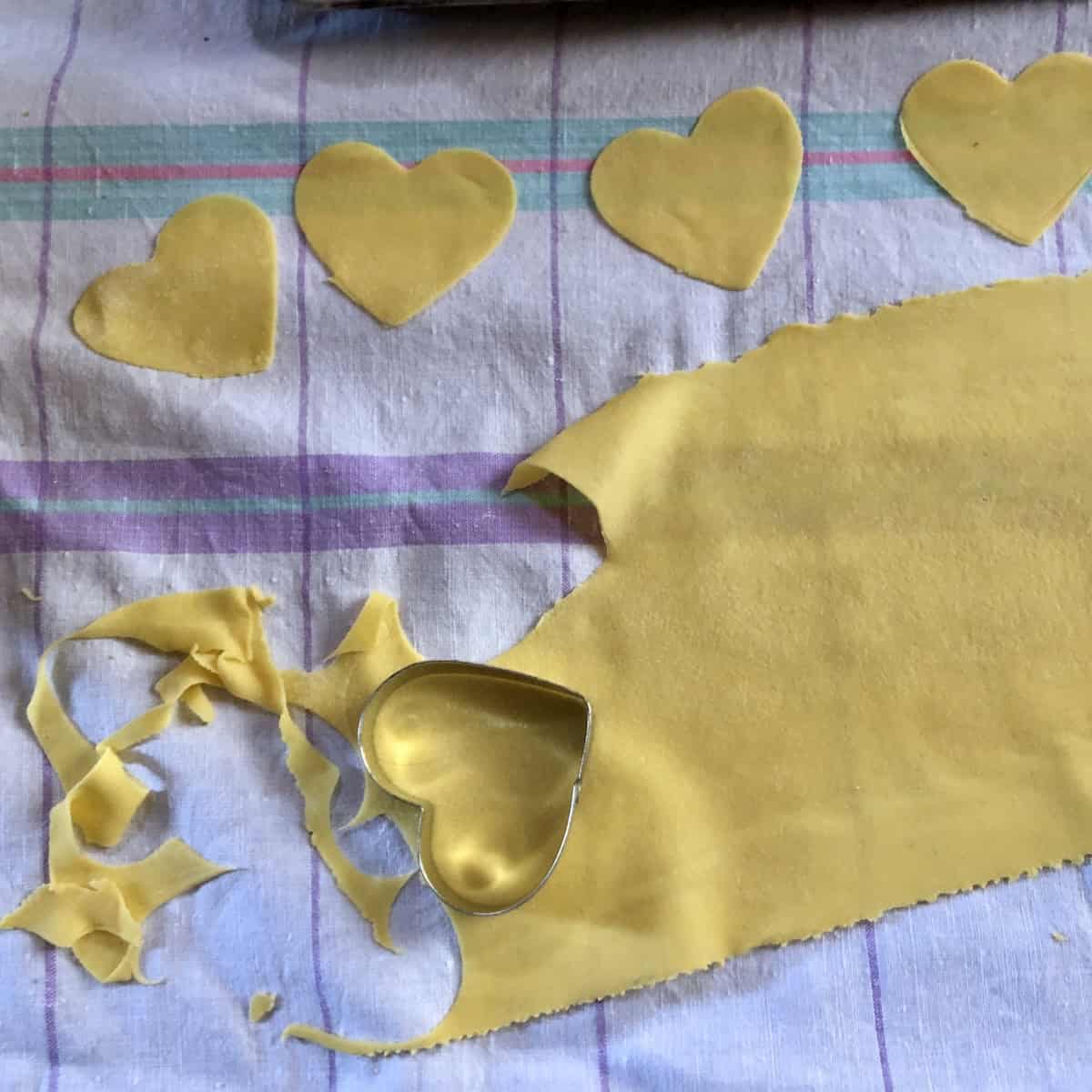 Homemade ravioli dough rolled out with heart shaped cookie cutter being used to create heart shaped lobster ravioli.
