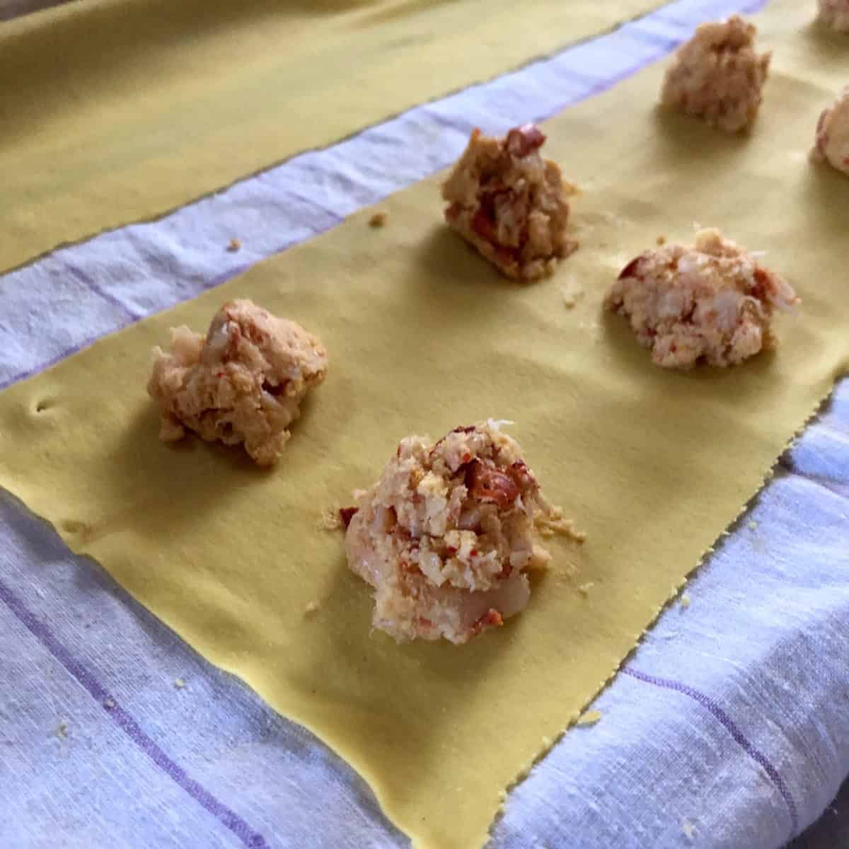 Homemade pasta sheet with dollops of lobster and shrimp ravioli filling showing large chunks of lobster meat and shrimp mousse before sealing, how to make lobster ravioli.
