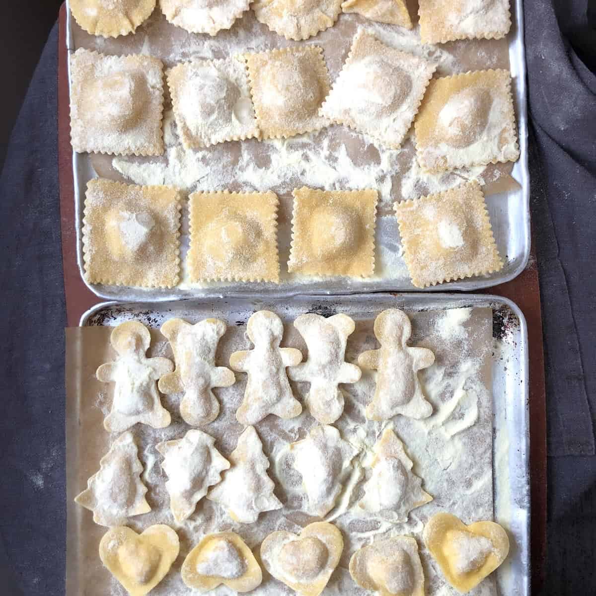 Filled round, square, heart shaped, turkey shaped, gingerbread men, Christmas tree, and star shaped lobster ravioli on parchment lined sheet tray dusted with semolina flour for meal prep freezing or same day cooking.
