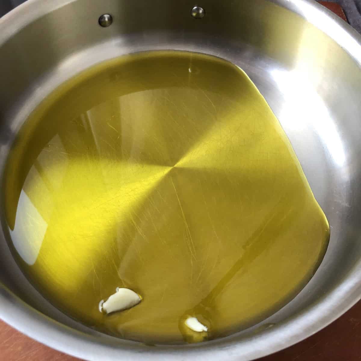 Smashed garlic cloves added to extra virgin olive oil in a skillet, the first step for making authentic Italian pasta ai funghi to perfume the EVOO.