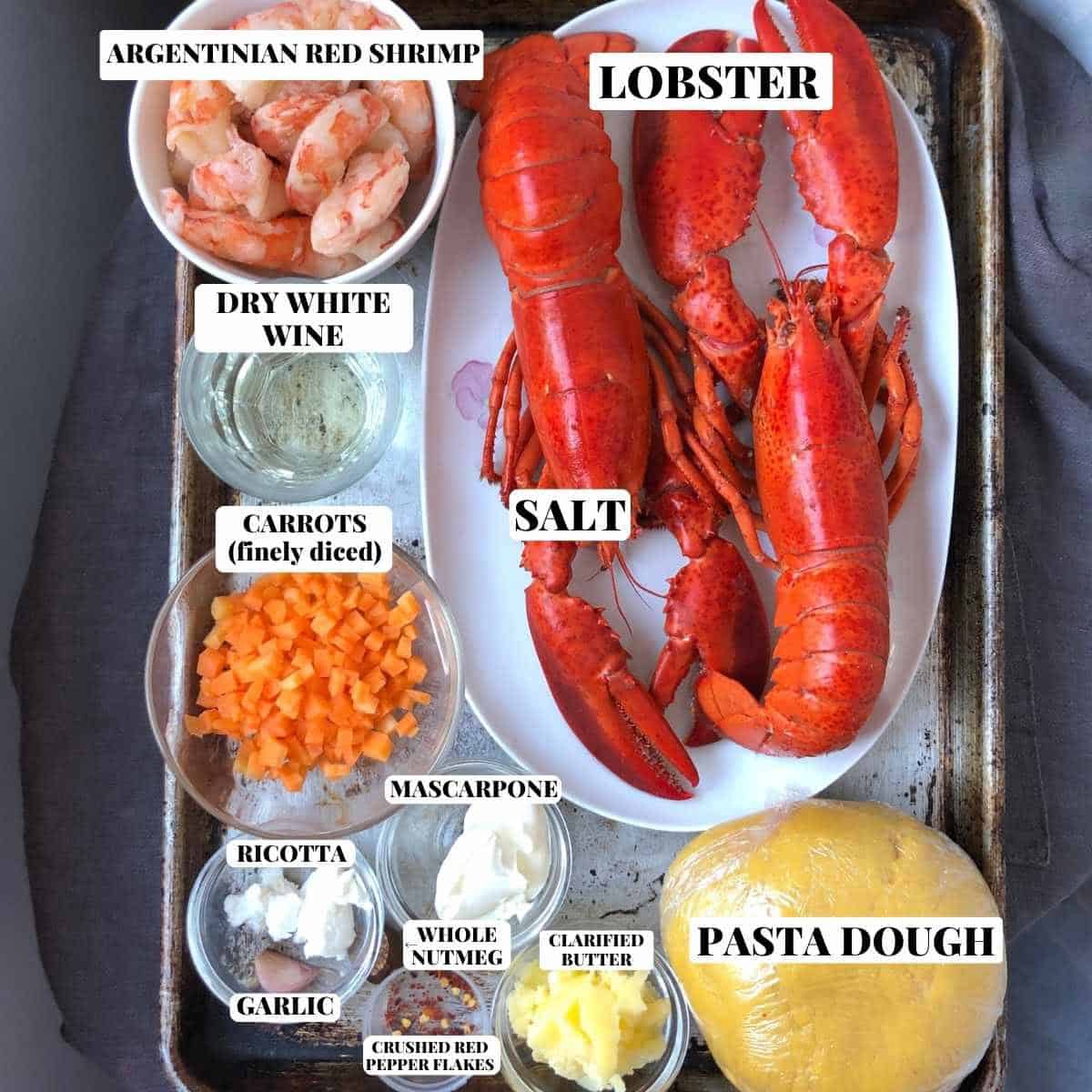 Lobster ravioli filling ingredients including homemade pasta dough on a baking sheet including lobster meat, argentinean red shrimp, mascarpone, ricotta, white wine, garlic, finely diced carrots, clarified butter, crushed red peppers, and whole nutmeg for the best homemade lobster ravioli recipe.
