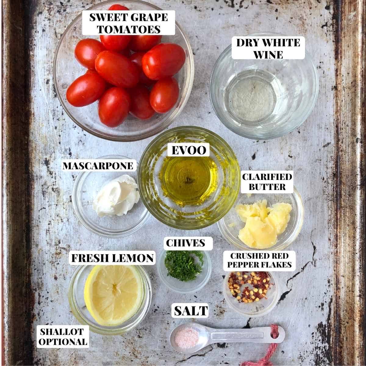 Lobster tomato cream sauce ingredients labeled on a baking sheet including grape tomatoes, mascarpone cheese, white wine, garlic, olive oil, and clarified butter for lobster ravioli sauce recipe.
