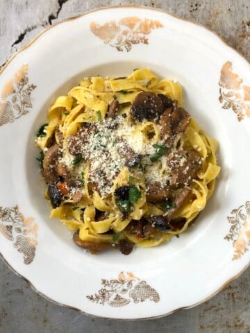 Authentic Italian pasta ai funghi in a white bowl topped with grated Grana Padano, a traditional mushroom pasta recipe made without cream.