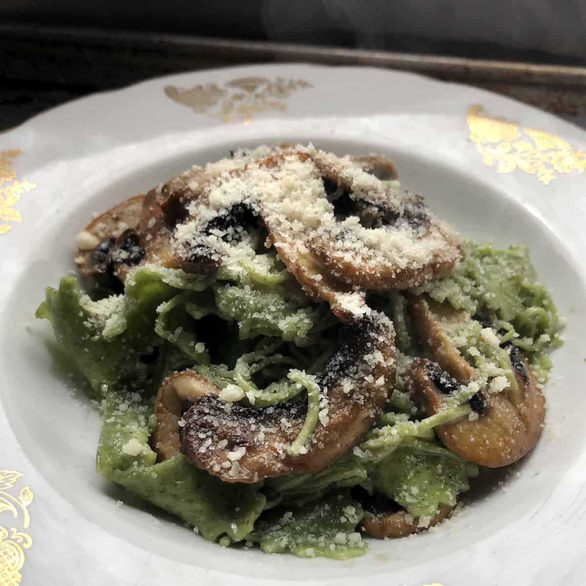 Homemade spinach pappardelle pasta ai funghi with sautéed mushrooms and grated Grana Padano garnish in a pasta bowl.
