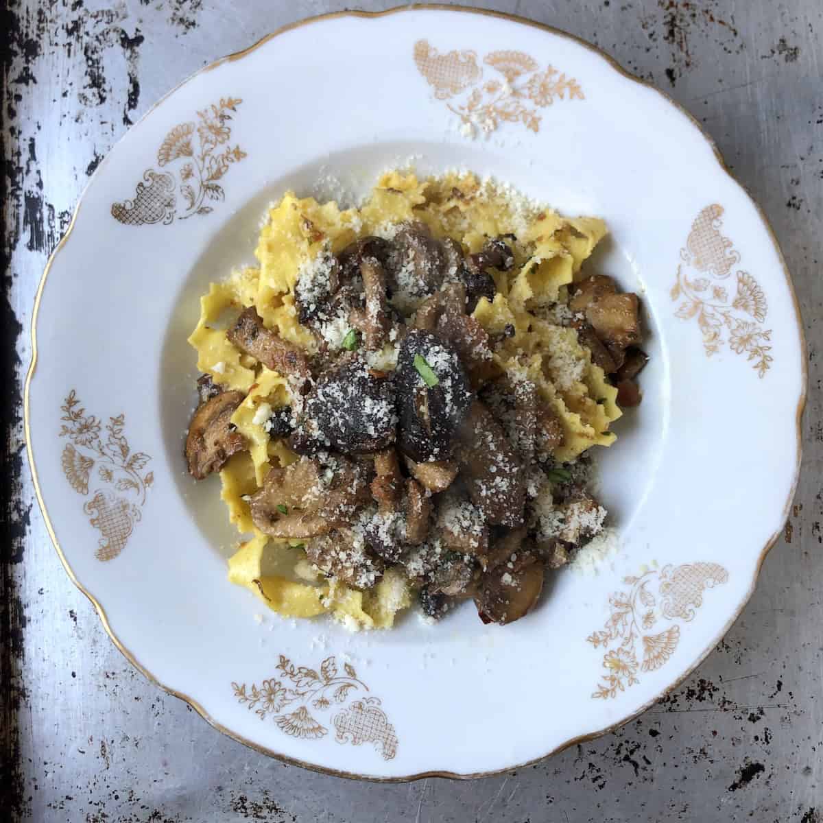 Fully assembled pasta ai funghi garnished with grated Grana Padano and fresh parsley, a traditional Italian mushroom pasta dish ready to serve.
