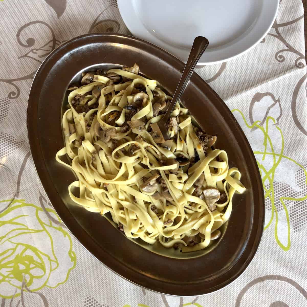 A large serving dish of mushroom pasta (pasta ai funghi) at one of our favorite restaurant in Northern Italy, showing how simple Italian mushroom pasta looks but tastes extraordinary.
