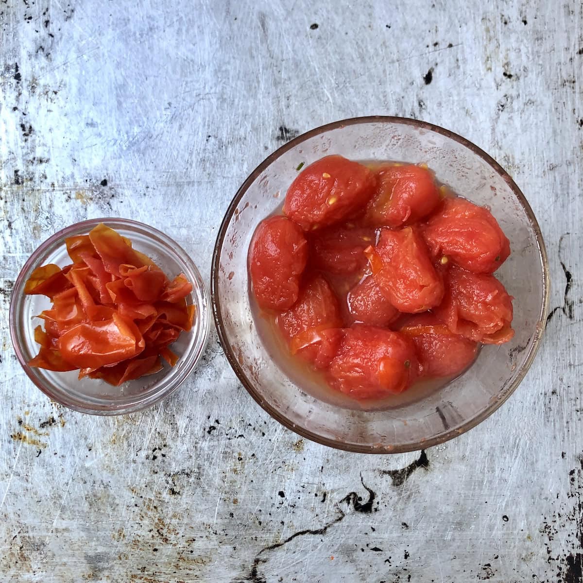 Tomato peels removed in separate bowl next to whole peeled grape tomatoes for lobster tomato cream sauce recipe.
