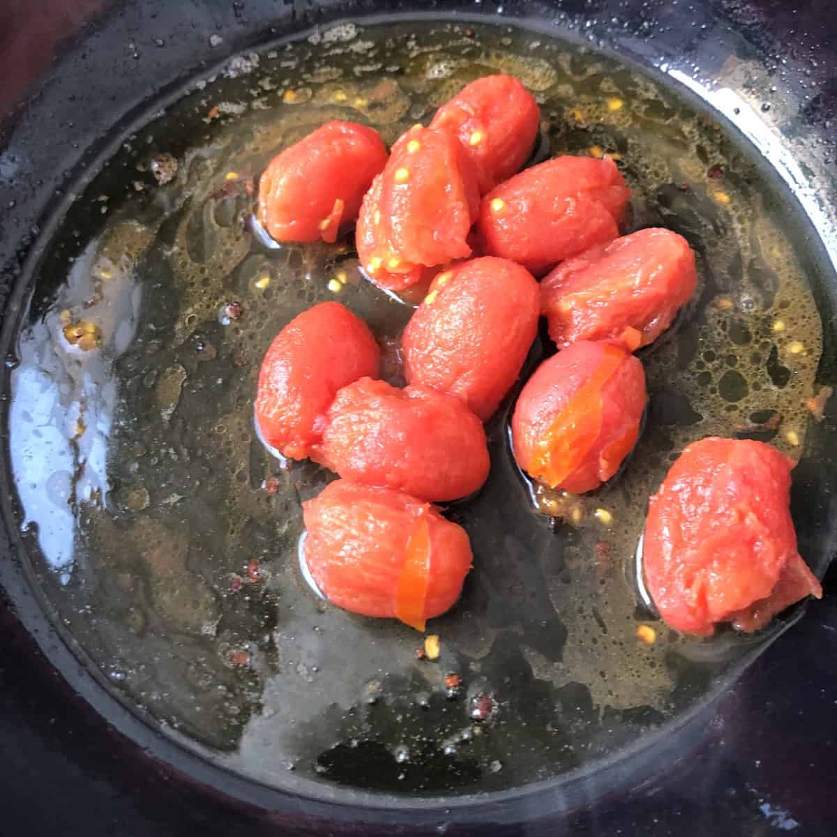 Adding peeled grape tomatoes to olive oil butter garlic mixture for lobster ravioli tomato cream sauce recipe.
