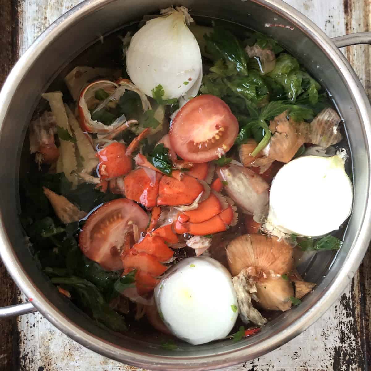 Quick seafood stock ingredients in a pressure cooker including roasted lobster and shrimp shells, onion, carrot, celery, tomato, and peppercorns for lobster ravioli recipe.