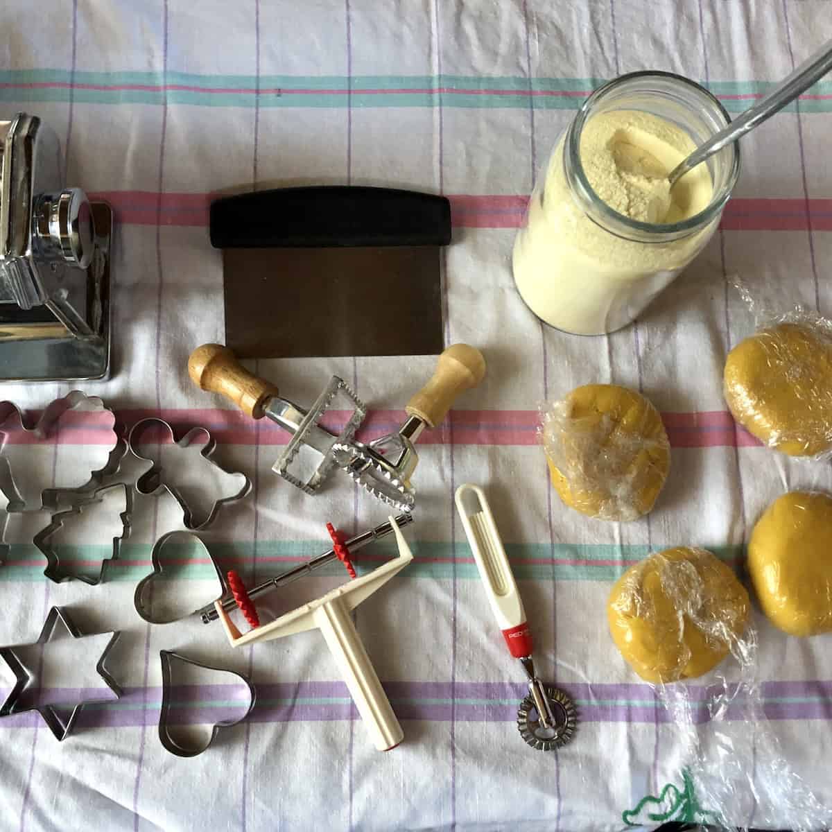 Ravioli making equipment including Atlas Marcato pasta machine, pasta bike cutters, cookie cutters, semolina flour for dusting, and bench scraper for homemade lobster ravioli.
