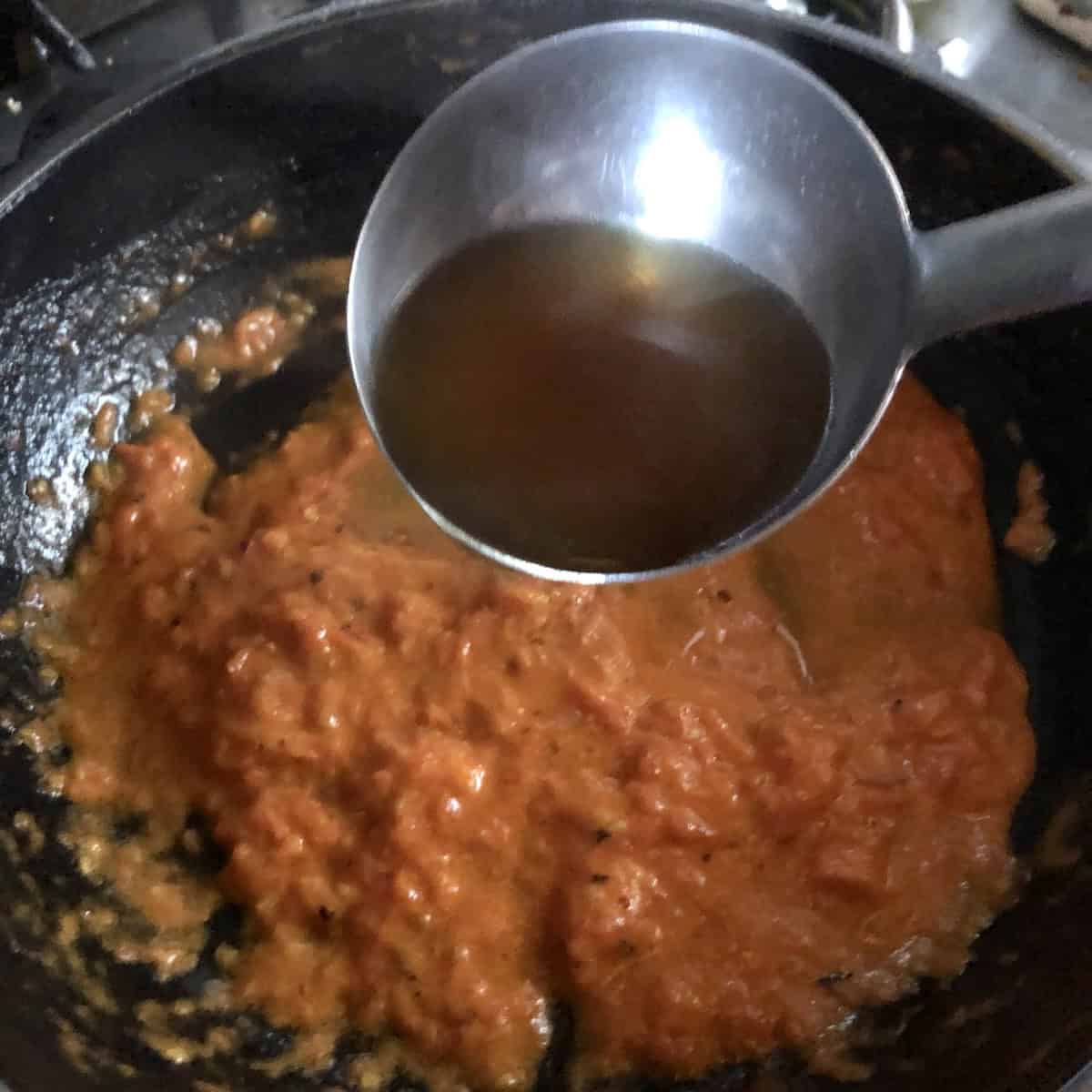 Adding starchy seafood stock to lobster tomato cream sauce to finish and loosen using the mantecare method for lobster ravioli sauce recipe.
