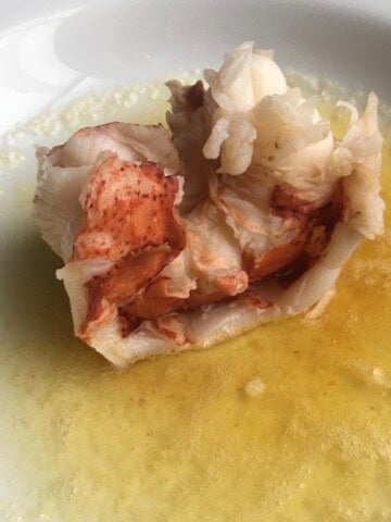 A perfectly boiled lobster tail sitting in a pool of warm clarified butter, showing the bright red and white tender lobster meat. An easy and elegant lenten seafood dinner in just 4 minutes.