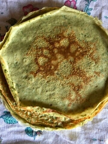 Light green basil and Parmigiano savory crepes stacked and ready to fill, showing the natural green color from fresh basil blended into the batter. A versatile meatless lenten breakfast or dinner crepe.