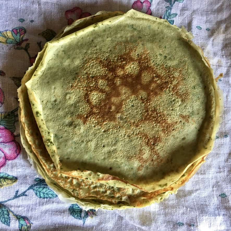 Light green basil and Parmigiano savory crepes stacked and ready to fill, showing the natural green color from fresh basil blended into the batter. A versatile meatless lenten breakfast or dinner crepe.