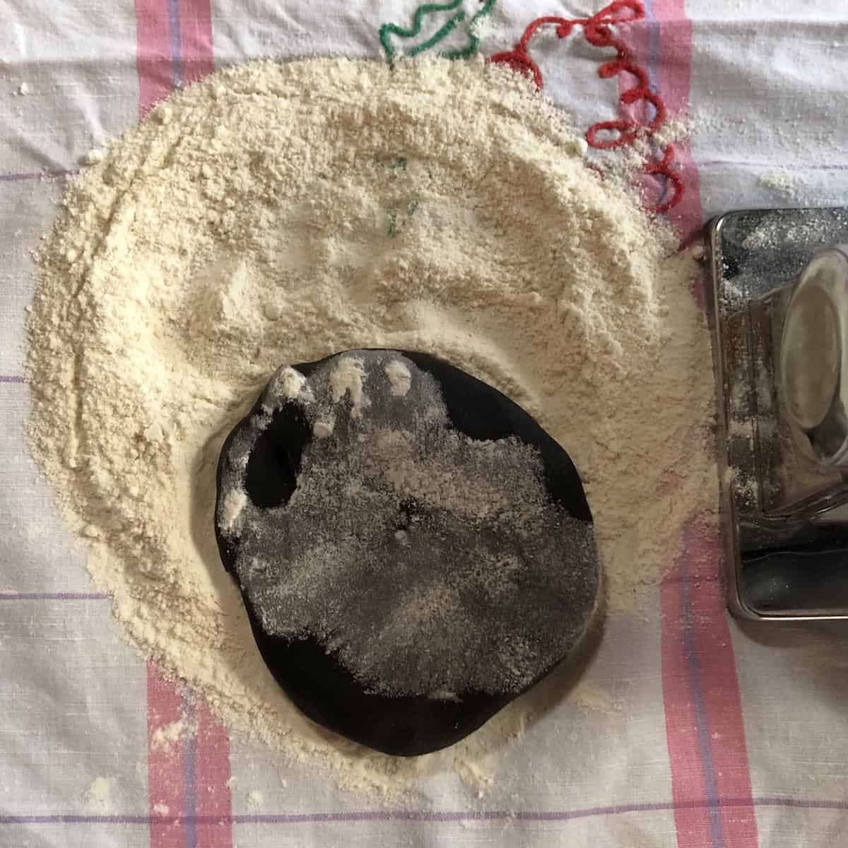 Flattened black pasta dough dusted with flour ready to roll through Marcato Atlas pasta machine on widest setting for homemade squid ink pasta.