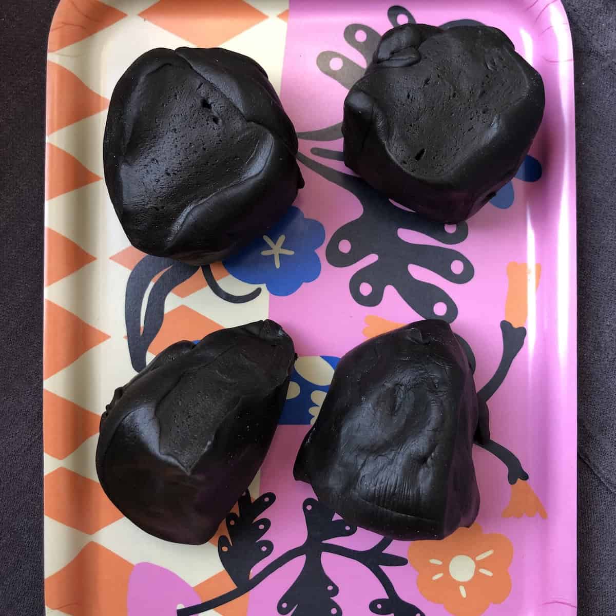 Four jet black squid ink pasta dough balls portioned and ready to roll and cut, homemade cuttlefish ink pasta recipe showing what does squid ink pasta taste like with this authentic Italian nero di seppia dough.