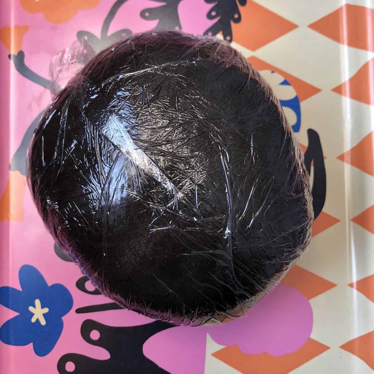 Fully black squid ink pasta dough ball with cuttlefish ink completely incorporated showing smooth jet black nero di seppia dough ready to rest and wrapped in sustainable cling film.