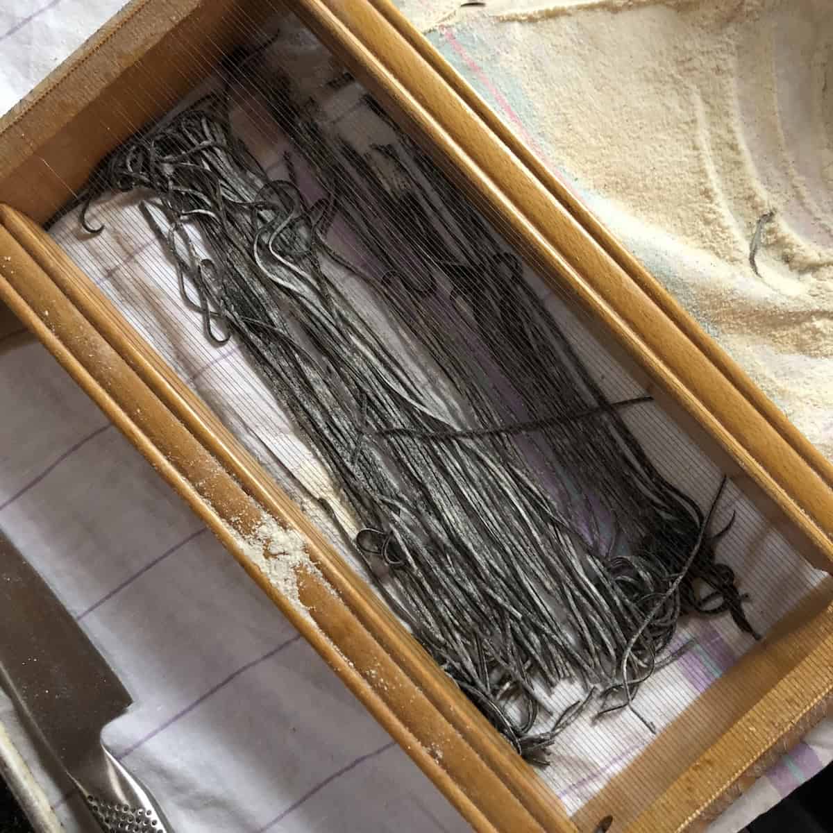 Fresh cut black spaghetti alla chitarra just passed through chitarra cutter ready to fold into nests for homemade squid ink noodles.
