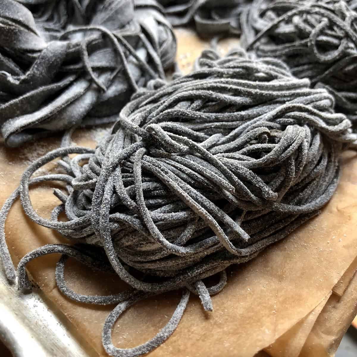 Black spaghetti alla chitarra nests dusted with flour on tray ready to cook or freeze, fresh squid ink noodles for nero di seppia pasta.
