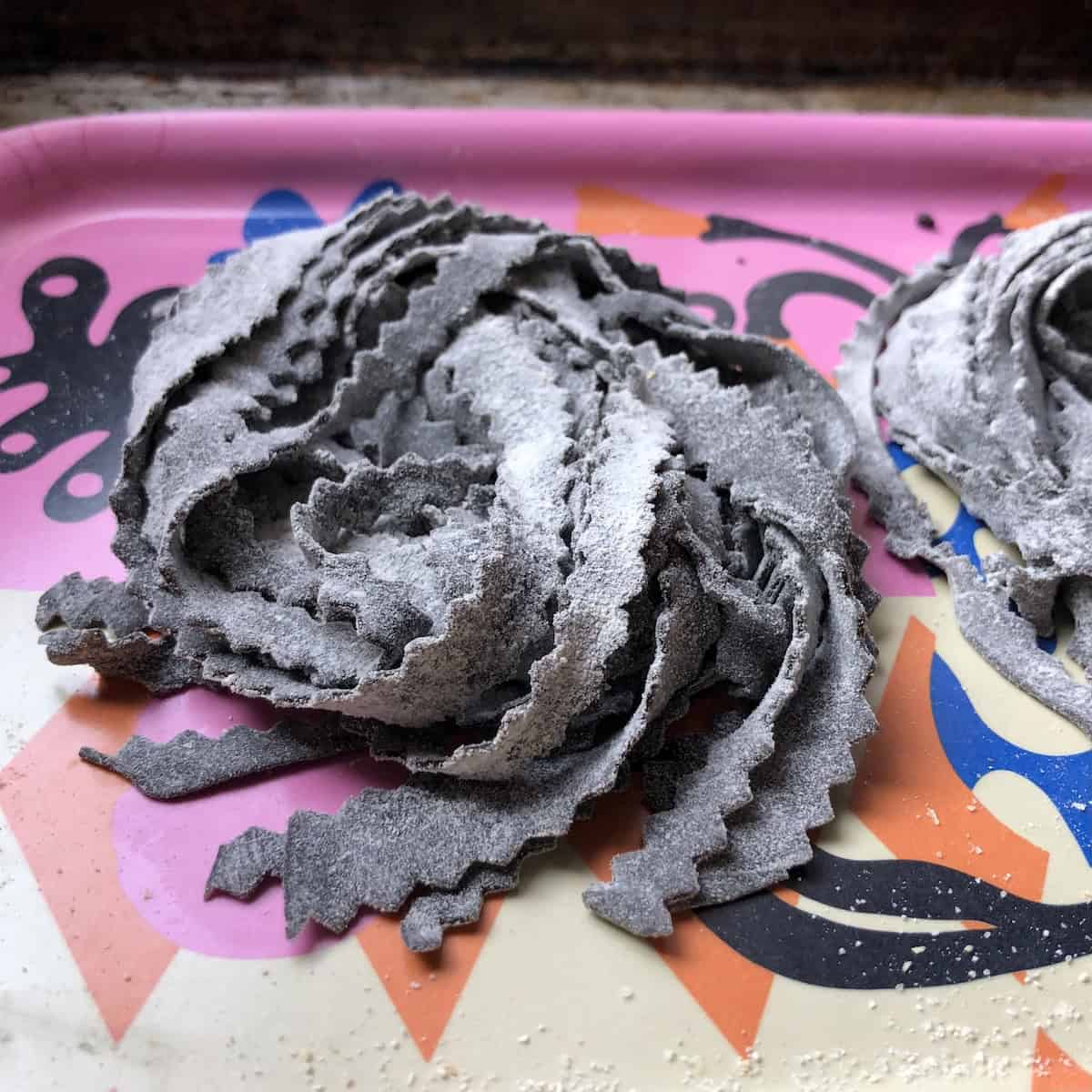 Homemade black tagliatelle reginelle with zigzag edges in nests dusted with flour, fresh squid ink pasta ready for seafood pasta dishes.
