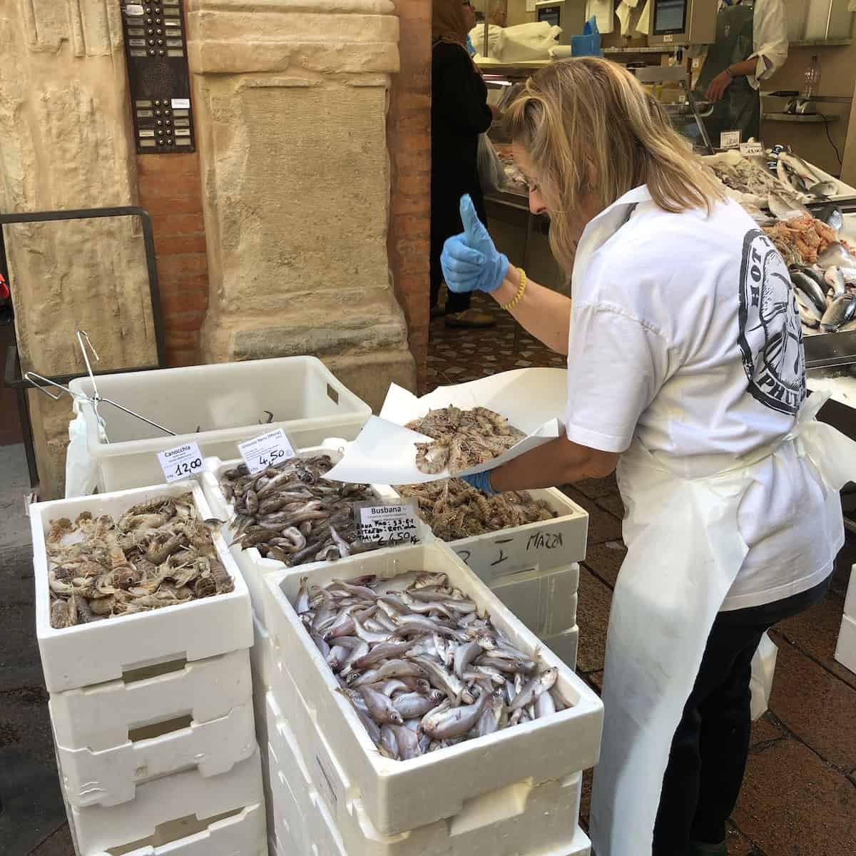 Bologna fishmonger serving fresh Italian shrimp for squid ink pasta with seafood sauce at famous fish market street.
