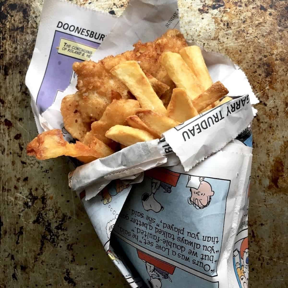 Traditional British fish and chips wrapped in comic strip newspaper, served the classic way with crispy battered fish and thick-cut chips. A fun and nostalgic lenten Friday dinner idea.