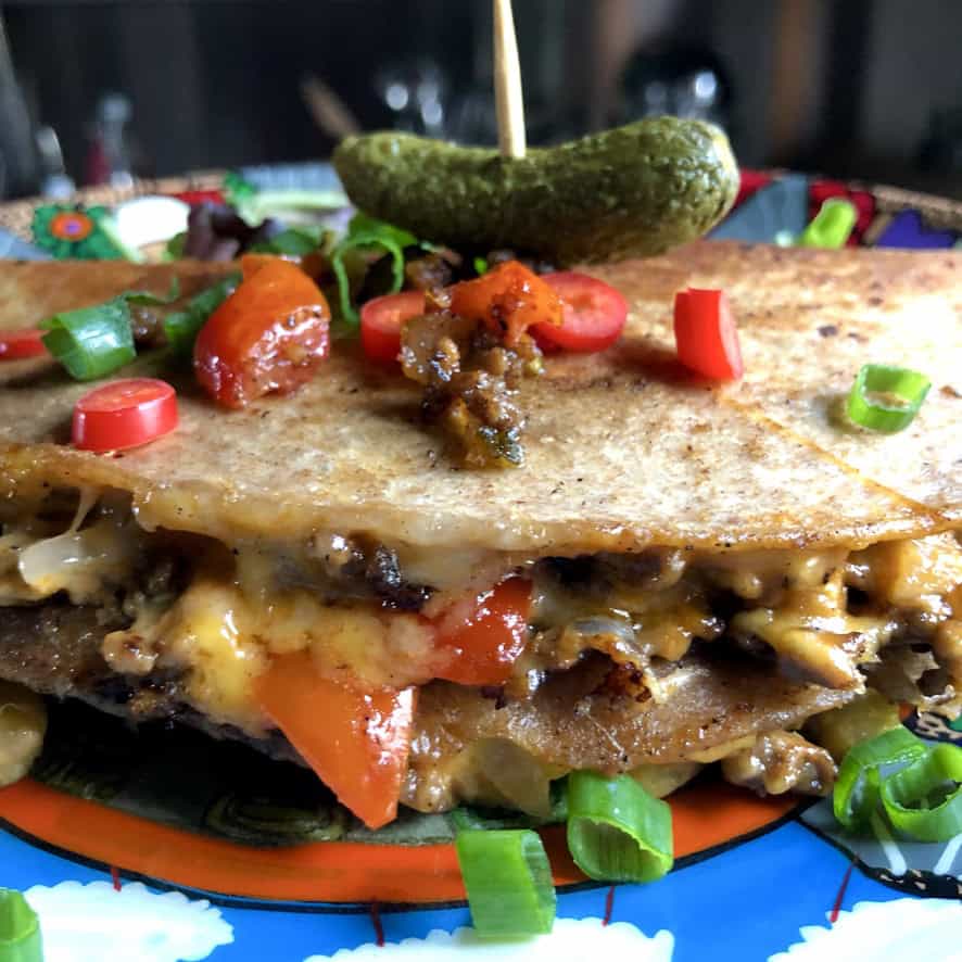 Cheeseburger quesadillas sliced into triangles on a cutting board, showing melted cheese and seasoned ground beef spilling from crispy golden tortillas. A fun family-friendly meatless lenten dinner using plant-based beef.