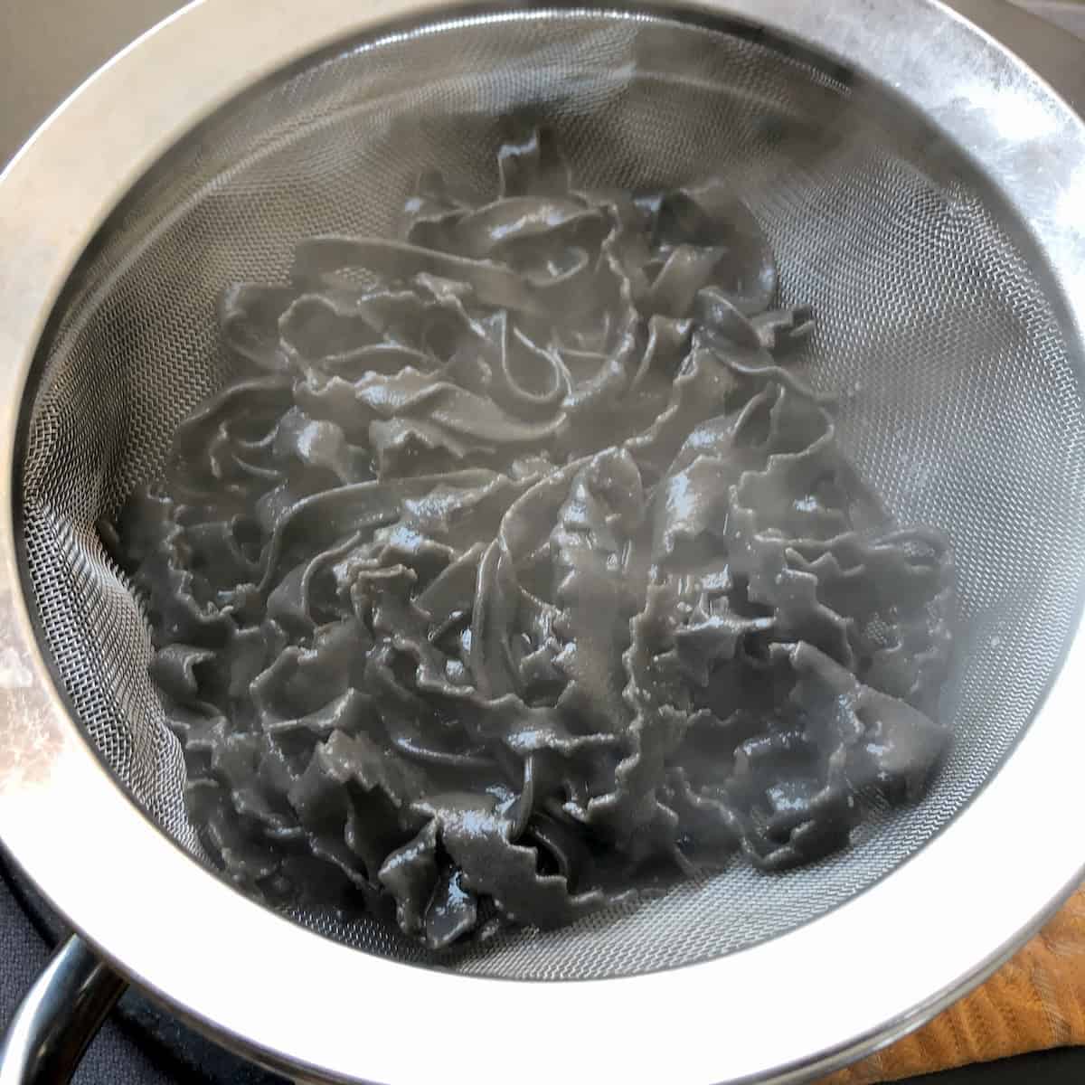 Cooked homemade black squid ink pasta in fine mesh strainer ready for sauce, fresh nero di seppia noodles for seafood pasta.
