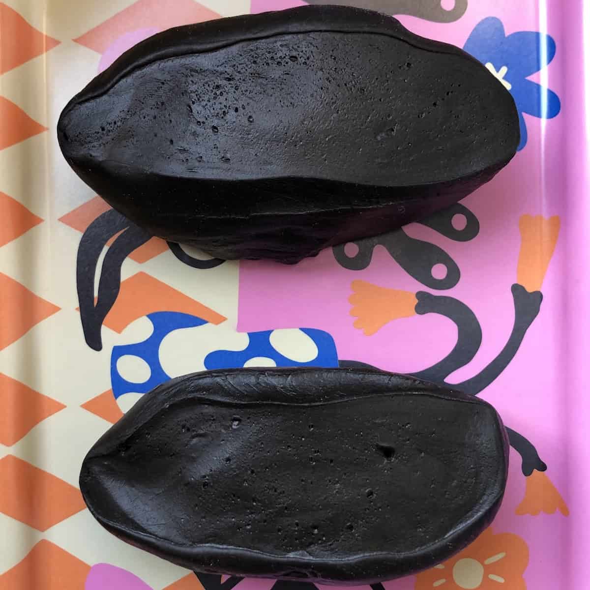 Two halves of black cuttlefish ink pasta dough ready to portion into four pieces for rolling homemade squid ink pasta.
