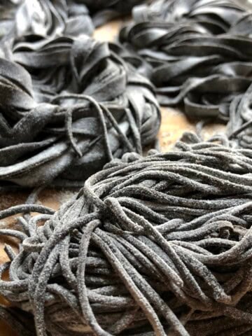 Close-up of homemade cuttlefish ink pasta nests in various shapes on tray, fresh black pasta ready for seafood pasta recipes and nero di seppia dishes.