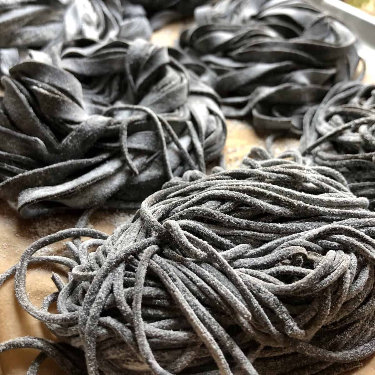 Close-up of homemade cuttlefish ink pasta nests in various shapes on tray, fresh black pasta ready for seafood pasta recipes and nero di seppia dishes.
