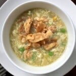 A bowl of homemade egg drop soup with crispy fried homemade wonton strips, green peas, corn, and sliced scallions showing how easy it is to make this Chinese soup at home.