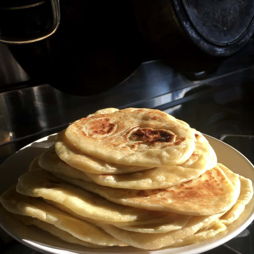 A platter piled high with super fluffy homemade naan bread, showing soft pillowy texture with golden brown spots from the cast-iron skillet. Perfect for scooping hummus and dips during Lent.